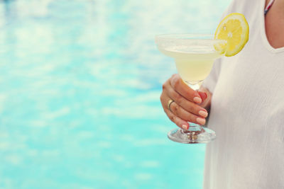 Midsection of woman holding drink by swimming pool