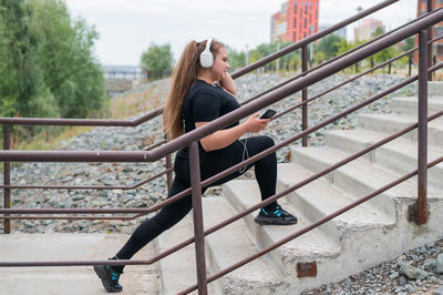 Side view of young woman sitting on railing