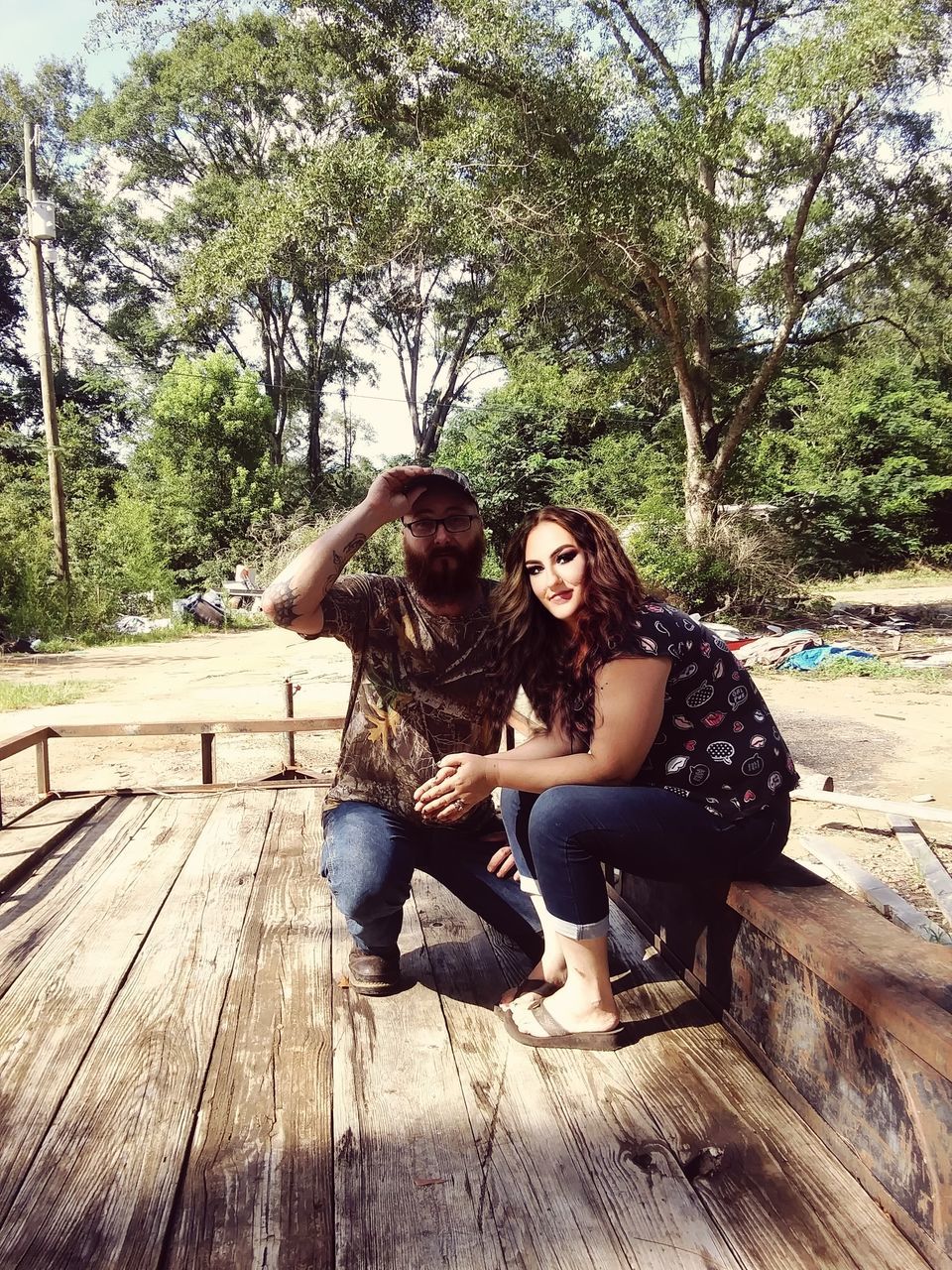 tree, sitting, young adult, adult, full length, two people, plant, women, wood, leisure activity, casual clothing, nature, togetherness, emotion, lifestyles, day, happiness, men, friendship, smiling, sunlight, front view, positive emotion, outdoors, portrait, bonding, person, relaxation, looking at camera, clothing, female, forest, photo shoot, love, enjoyment, fashion, bench, land, park