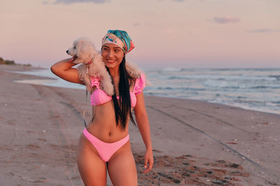 Smiling young woman in bikini with dog at beach