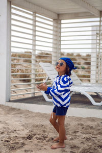 Boy child walks on the beach with sand on a chaise longue in a blue striped jacket and sunglasses