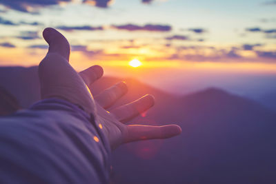 Cropped hand of person against sky during sunset