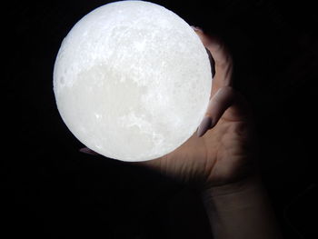 Cropped hand holding illuminated moon replica in darkroom