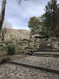 People walking on footpath by rocks against sky