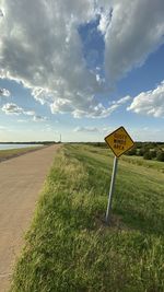 Road sign on field against sky