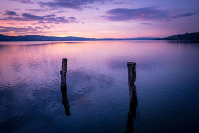 Wooden posts in lake against sky during sunset