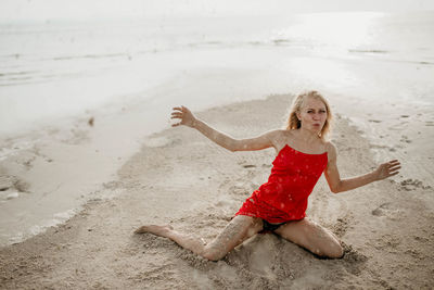 A girl in a red dress throws white sea sand