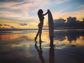 Reflection of woman on beach against sky during sunset