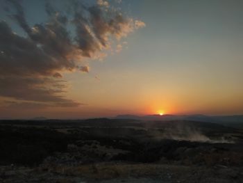 Scenic view of landscape against dramatic sky during sunset