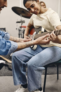 Full length of woman learning guitar from friend while rehearsing in classroom