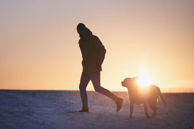 Rear view of man walking on beach against sky during sunset