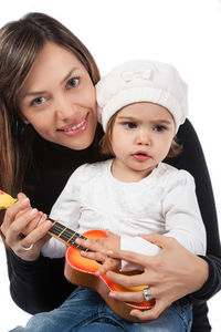 Portrait of happy mother with cute daughter holding toy guitar against white background