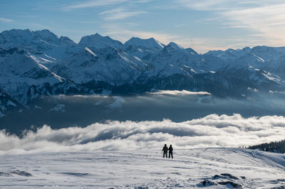 Rear view of people standing on snow covered land against mountain