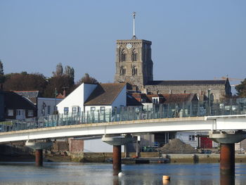 Bridge over river by buildings against clear sky