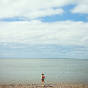 Rear view of girl walking on shore at beach against sky