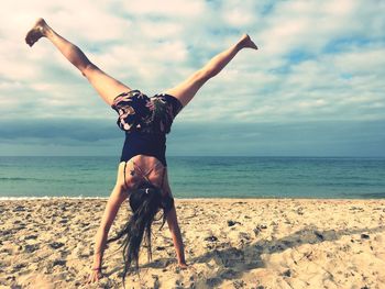 Full length of woman doing handstand on beach against sky
