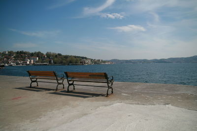 Empty bench on beach against sky