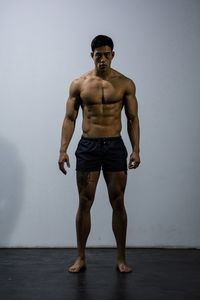 Portrait of shirtless muscular man standing against wall