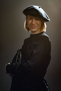 Young woman wearing hat standing against gray background