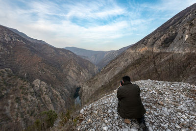 Man photographing mountains with camera against sky