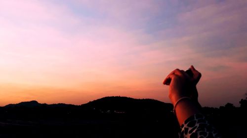 Midsection of silhouette person against orange sky