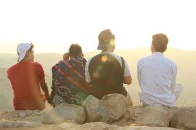 Rear view of people sitting on rock at mountain against sky