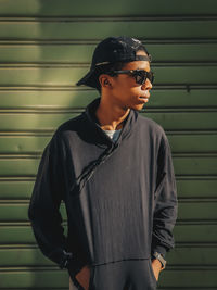 Young man wearing sunglasses standing against wall