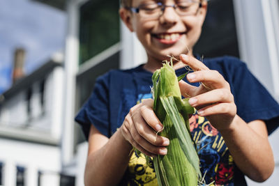 Low angle view of cheerful boy peeling corn on cob at yard