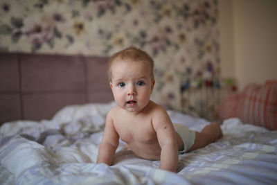 Charming baby of 6 months is lying on his stomach on a bed in a bright real interior,