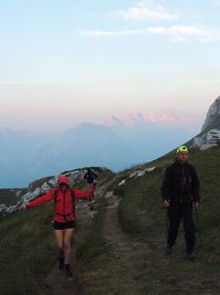 Man and woman hiking on mountain against sky during sunset