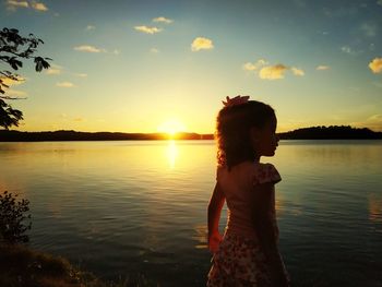 Woman standing by lake against sky during sunset