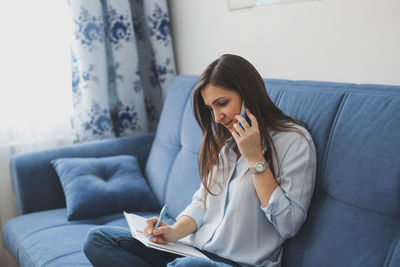 Young woman using mobile phone while lying on bed at home