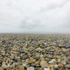 View of pebbles in calm sea against cloudy sky