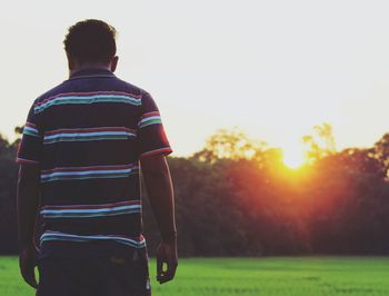 Rear view of man standing on field against sky during sunset