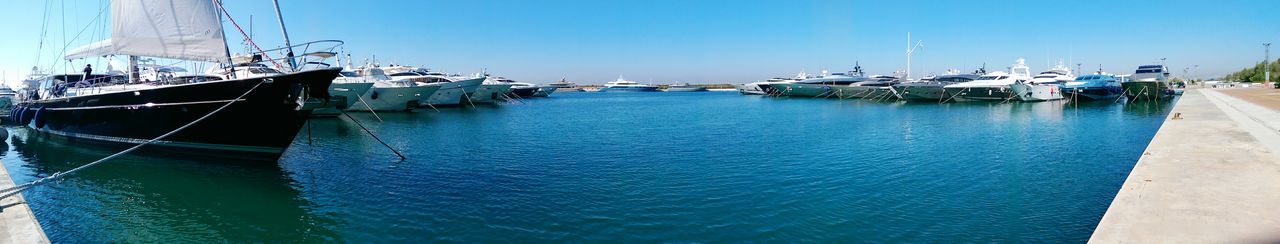 Sailboats moored at harbor against clear blue sky