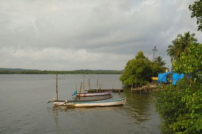 Boats moored in calm sea against cloudy sky