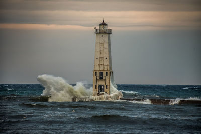 Lighthouse by sea against sky during sunset