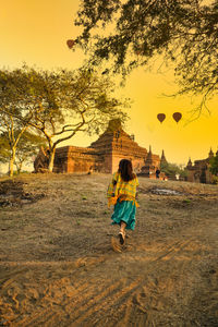 Rear view of woman walking on field against sky during sunset