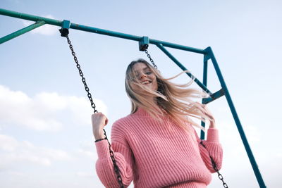 Young woman swinging against sky