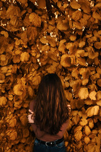 Rear view of woman standing amidst leaves during autumn
