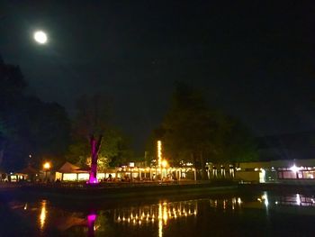 Illuminated city by lake against sky at night