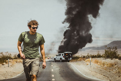Young man walking on road against burning car