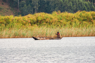 A tourist on a traditional fishing canoe at lake mutanda at sunset in kisoro town, uganda