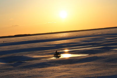 Silhouette people riding on sea against sky during sunset