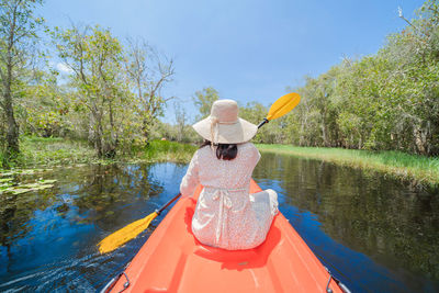 Rear view of woman on lake by trees against sky