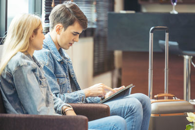 A couple sits in the hotel lobby, looking at a tablet computer.