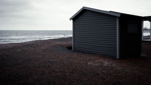 An old bathing hut on the beach, moody skies in the background. to the right a large crane. 