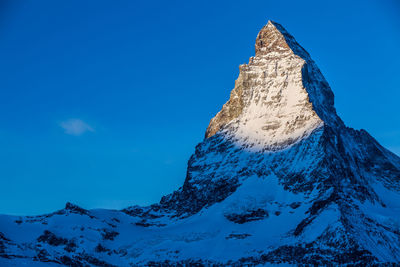 Low angle view of snowcapped mountains against clear blue sky