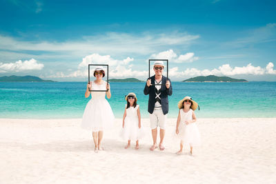 Full length of family standing on beach against sky