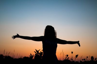 Silhouette woman with arms outstretched standing against clear sky during sunset